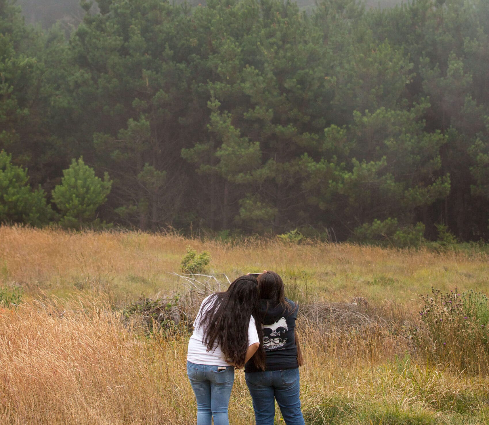 Two women standing in a field with a frisbee.