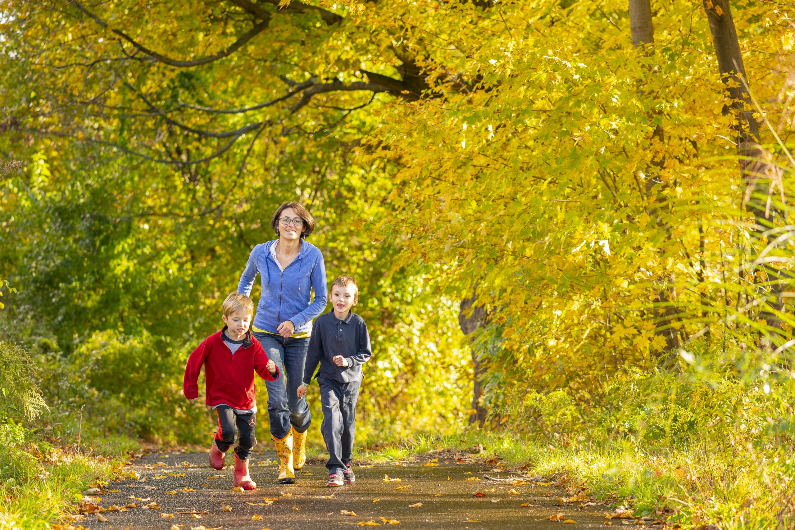 A woman and her children are running on a path in the fall.