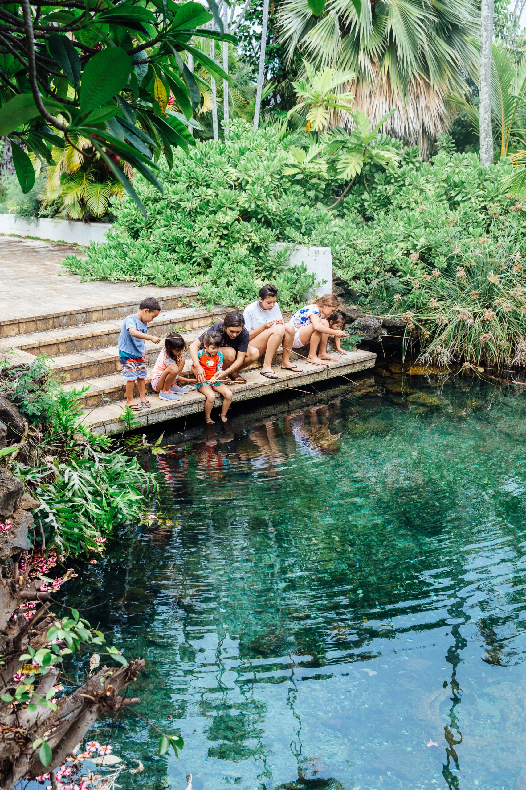 A group of children are sitting on the steps of a pond.