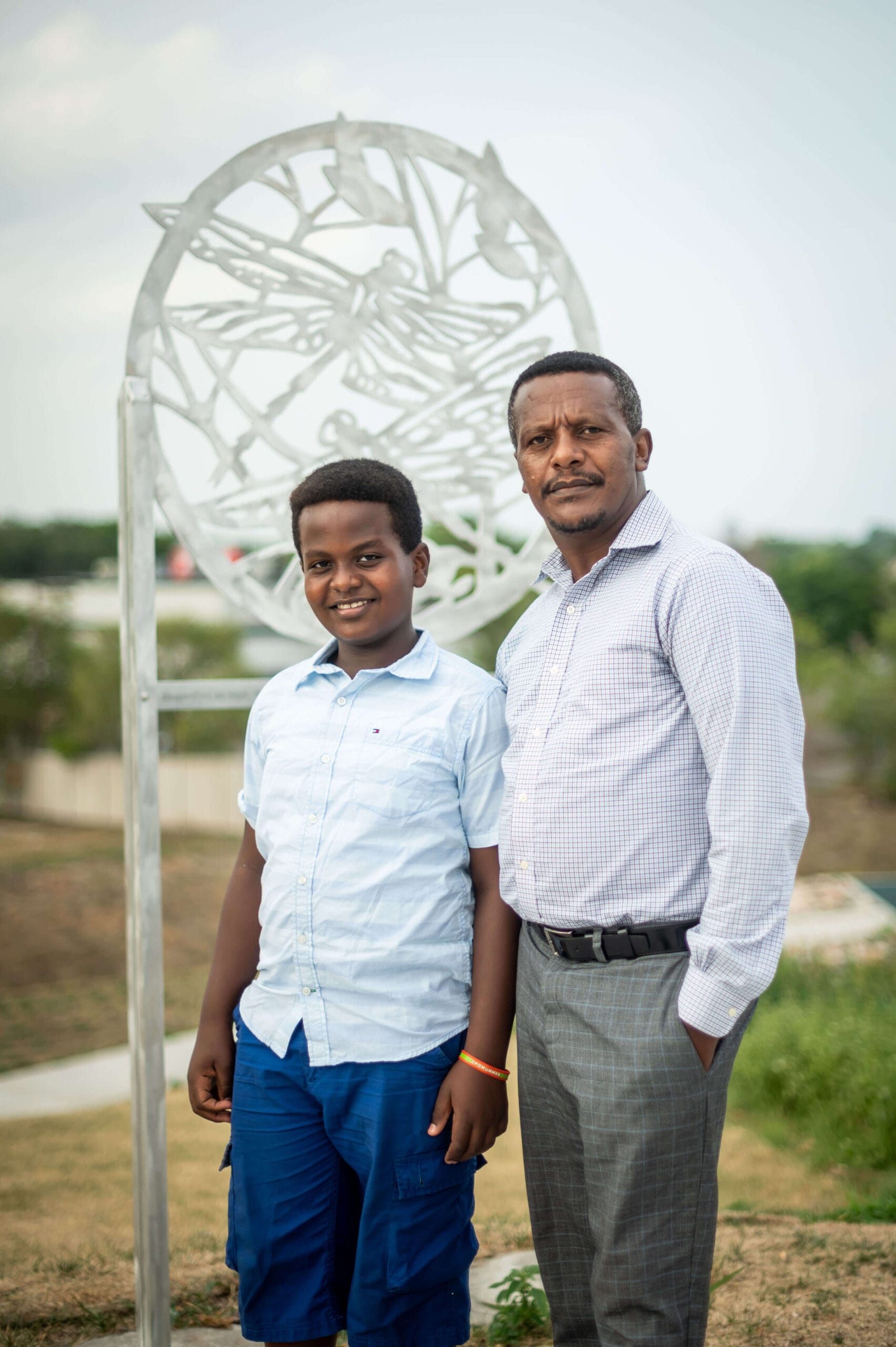 A father and son standing in front of a metal sculpture.