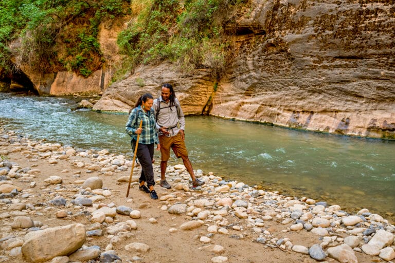 Two people standing next to a river in a canyon.