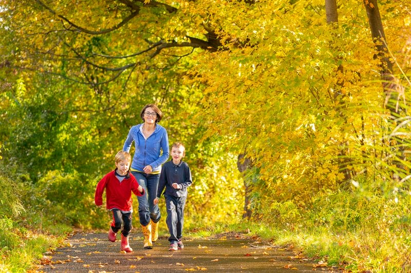 A woman and her children are running on a path in the autumn.
