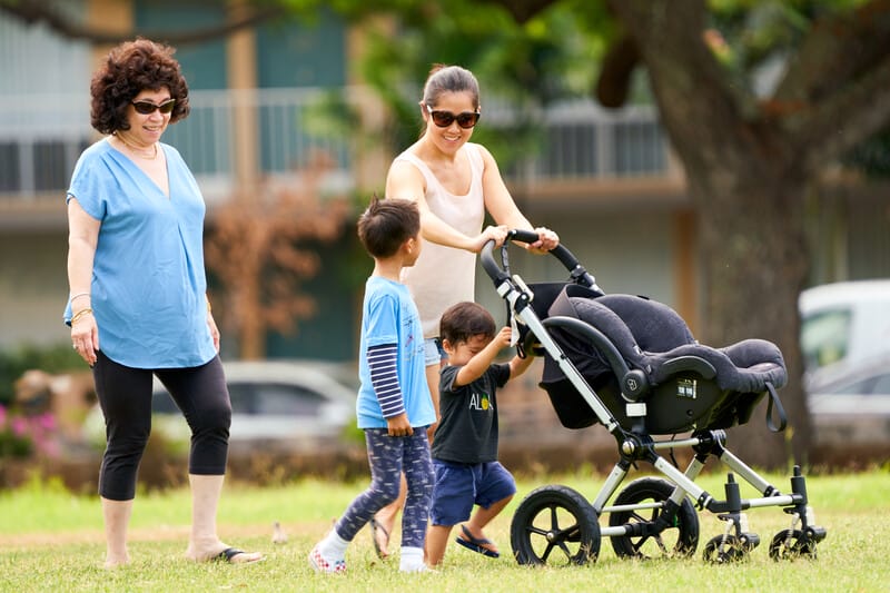 A woman and two children are pushing a stroller in a park.