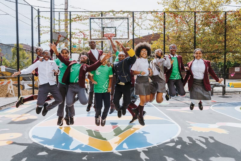 A group of school children jumping in the air on a basketball court.
