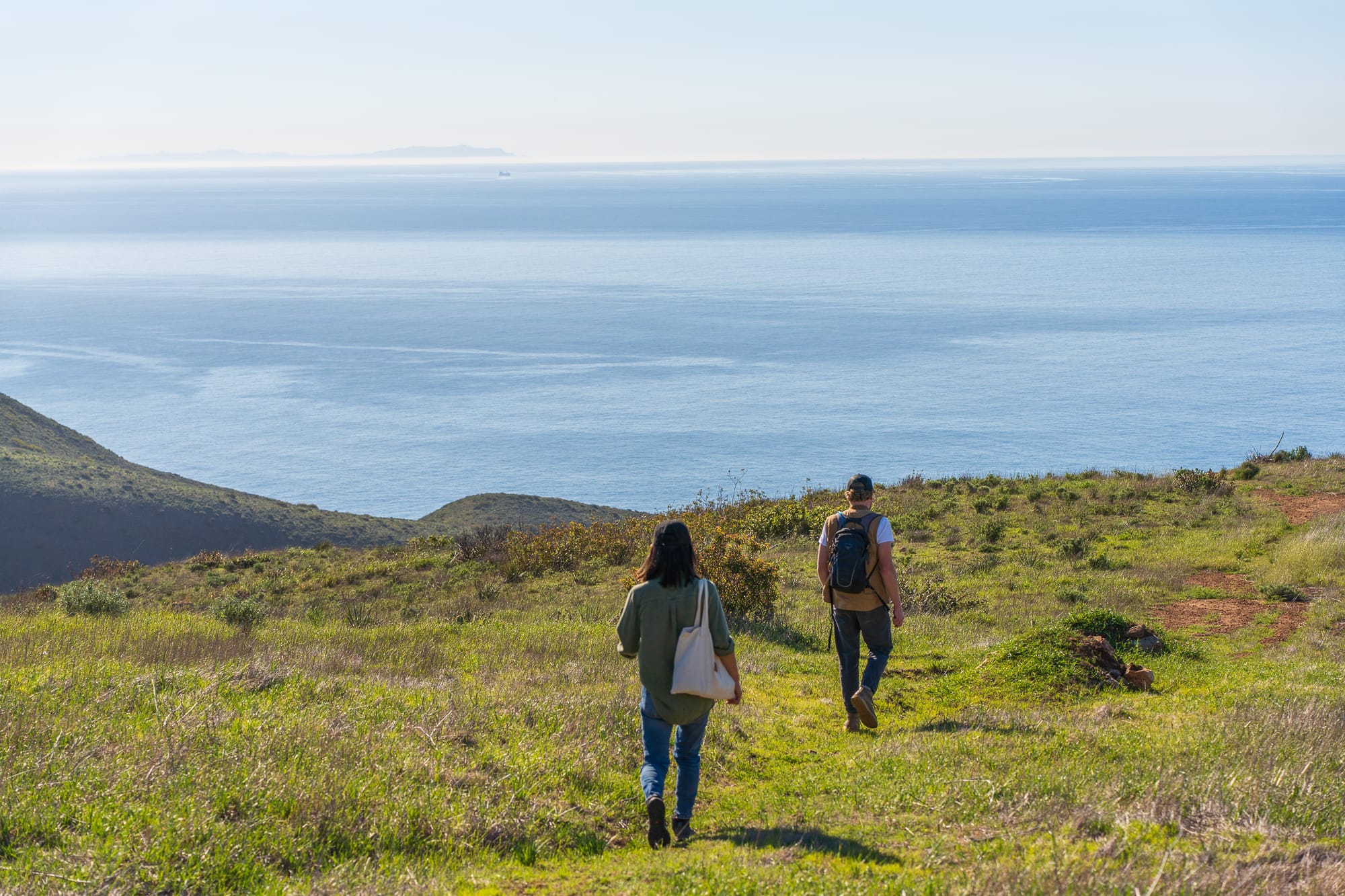 Two people walking down a hill next to the ocean.