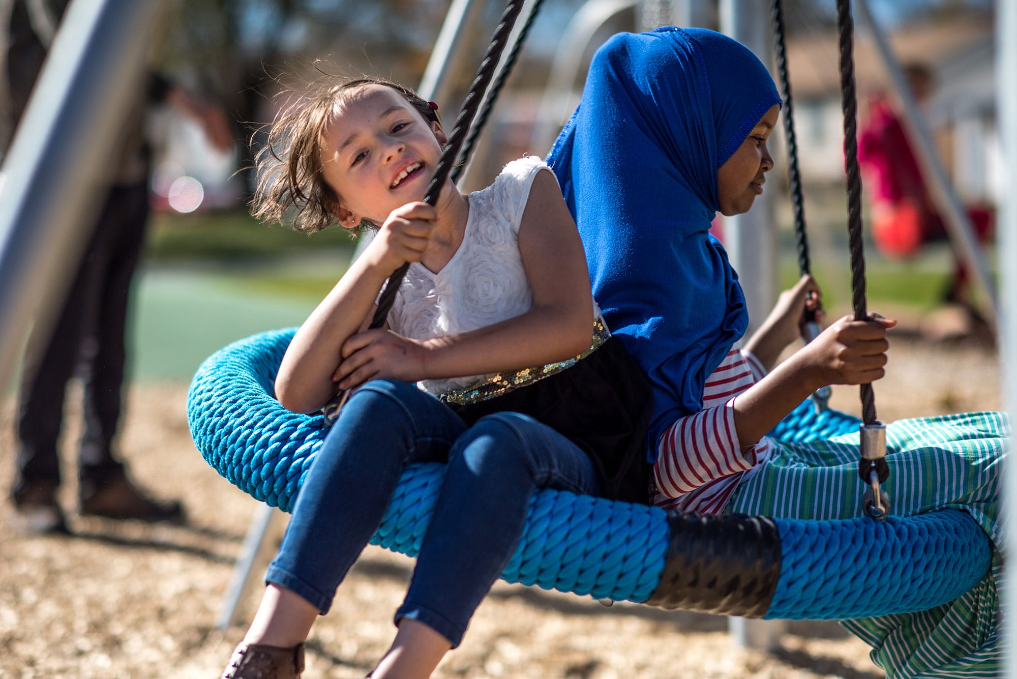 Two girls on a swing at a playground.