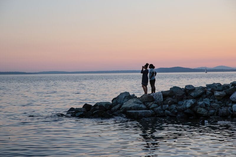 Two people standing on rocks in the water at sunset.