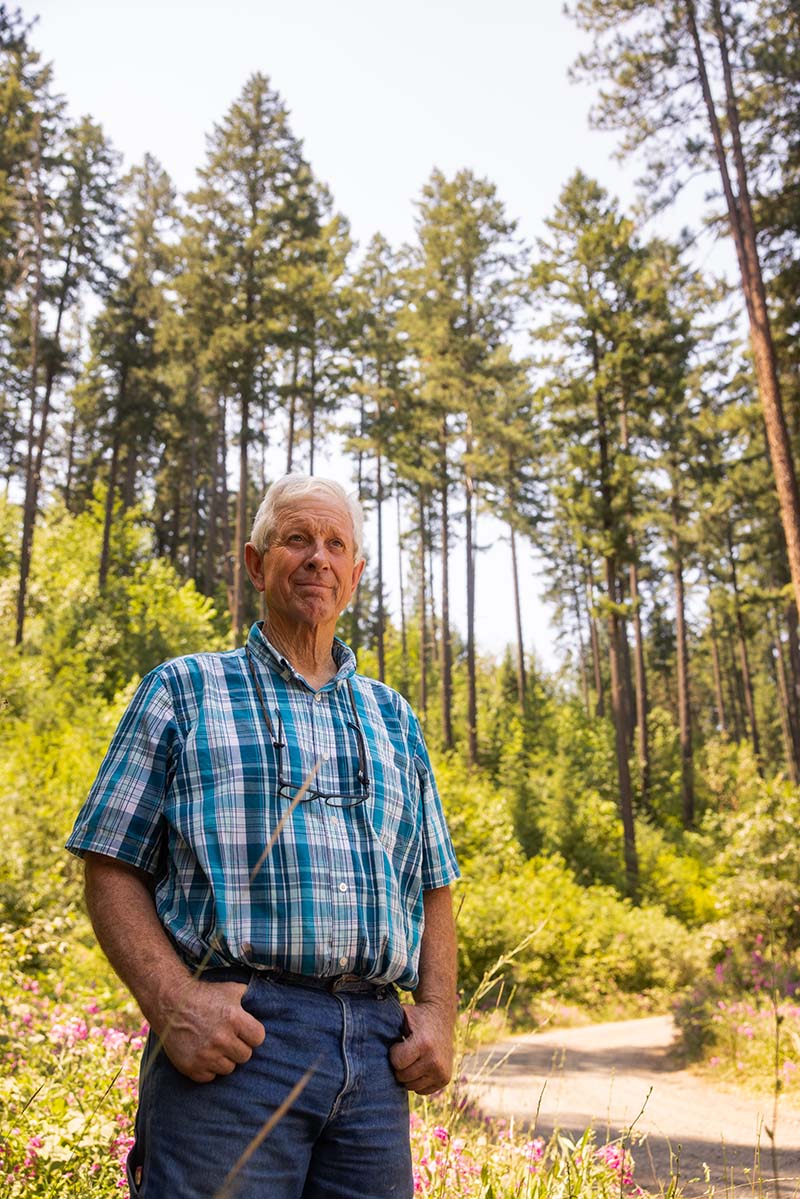 An older man standing in a wooded area.