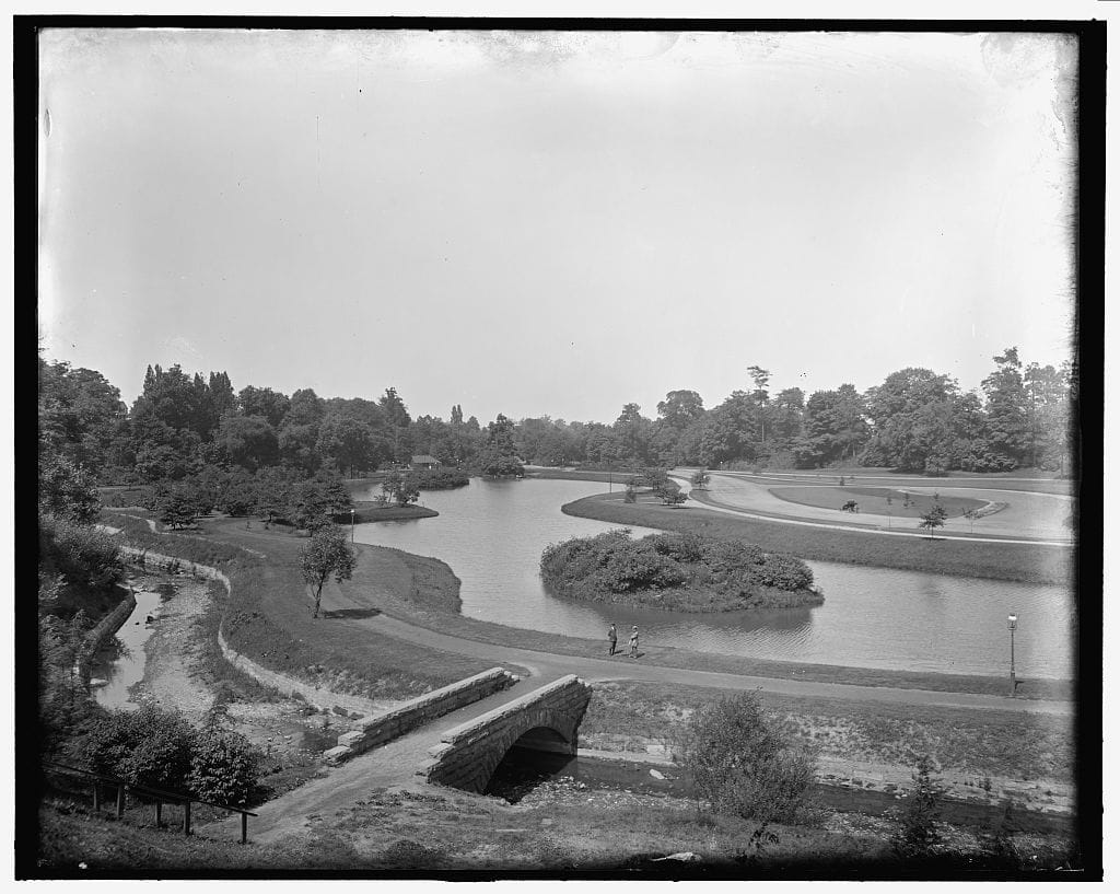 An old black and white photo of a park with a river.
