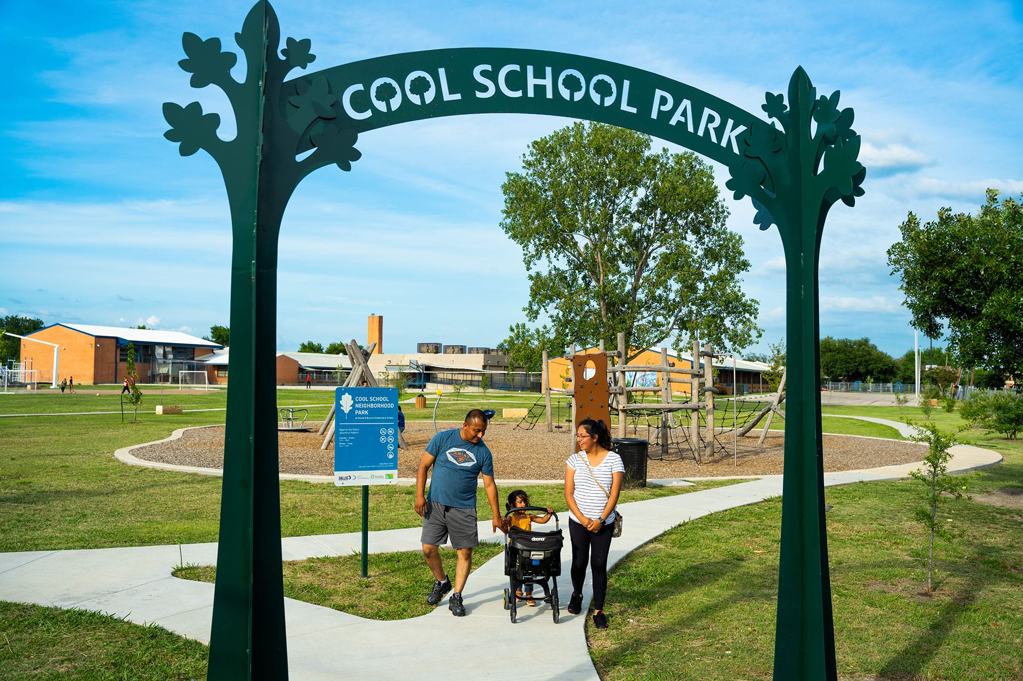 A family in a stroller in front of a sign that says cool school park.