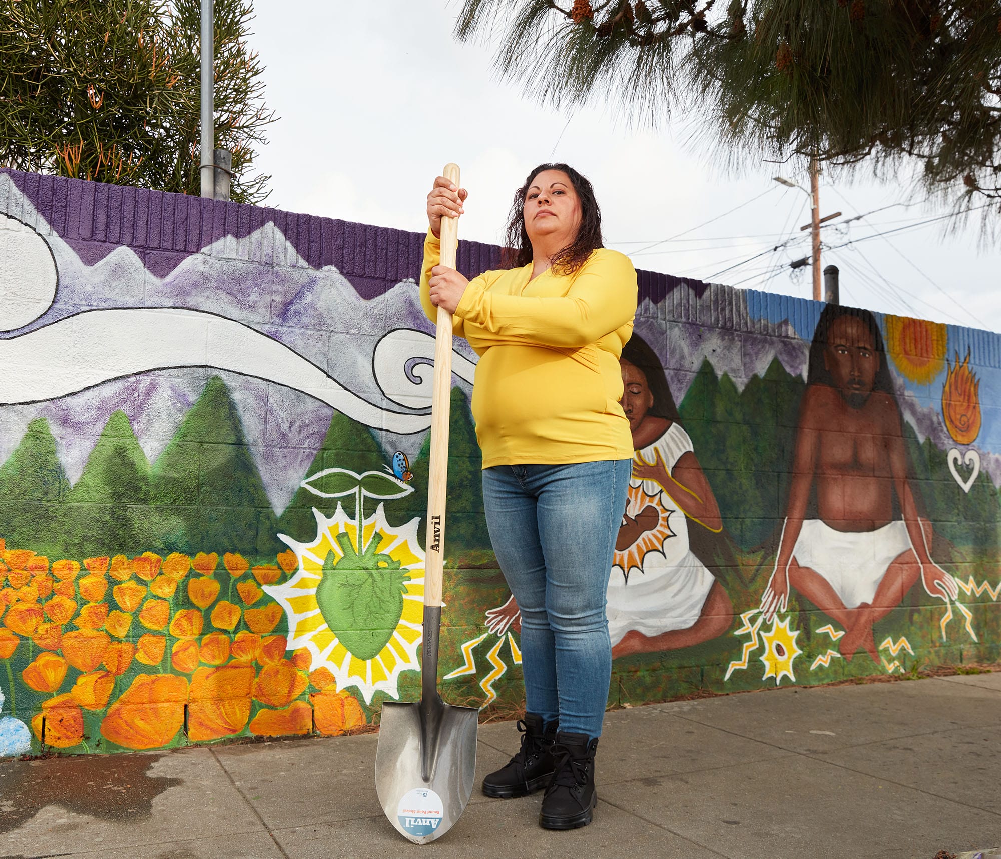 A woman holding a shovel in front of a mural.