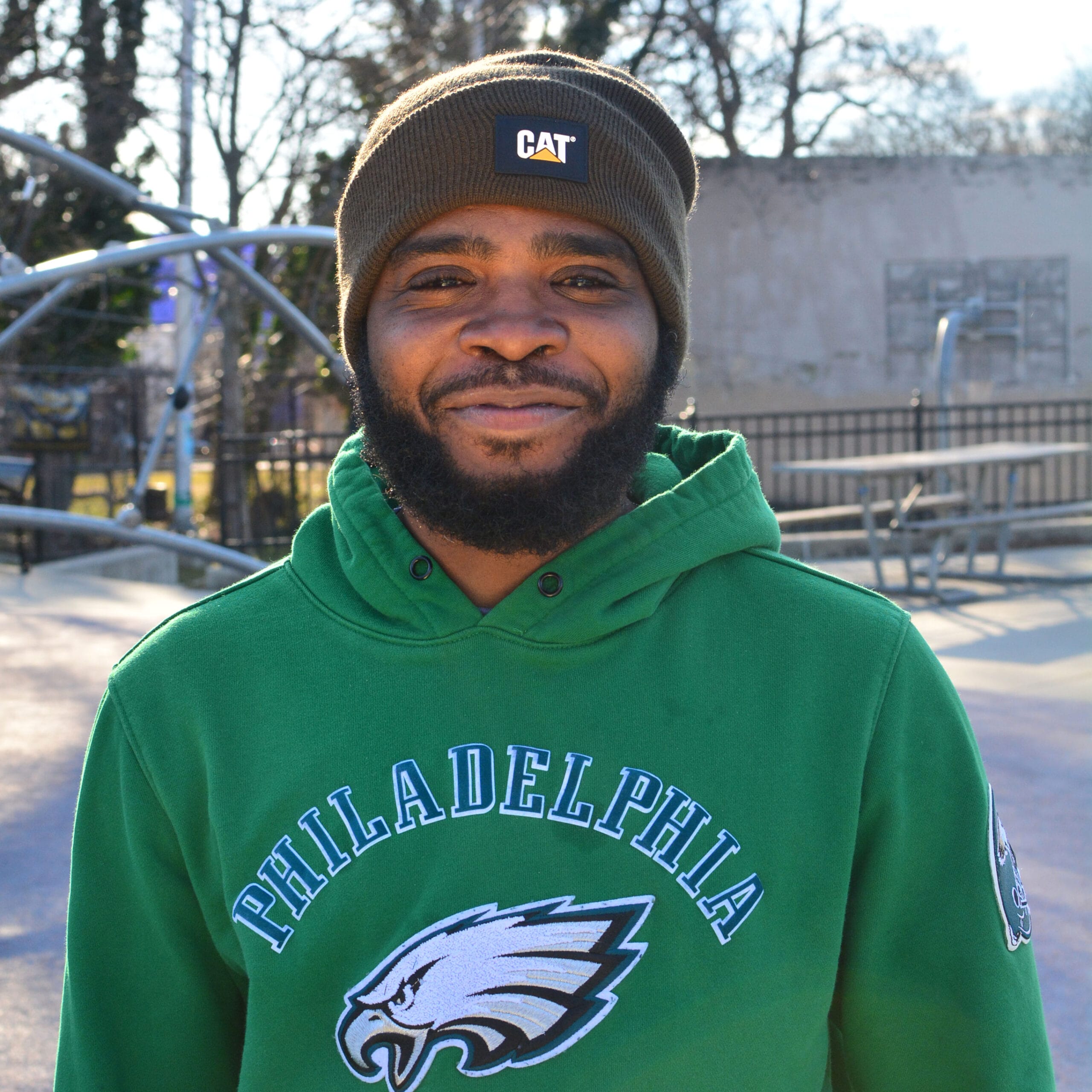 A young man in a green hoodie standing in front of a playground.