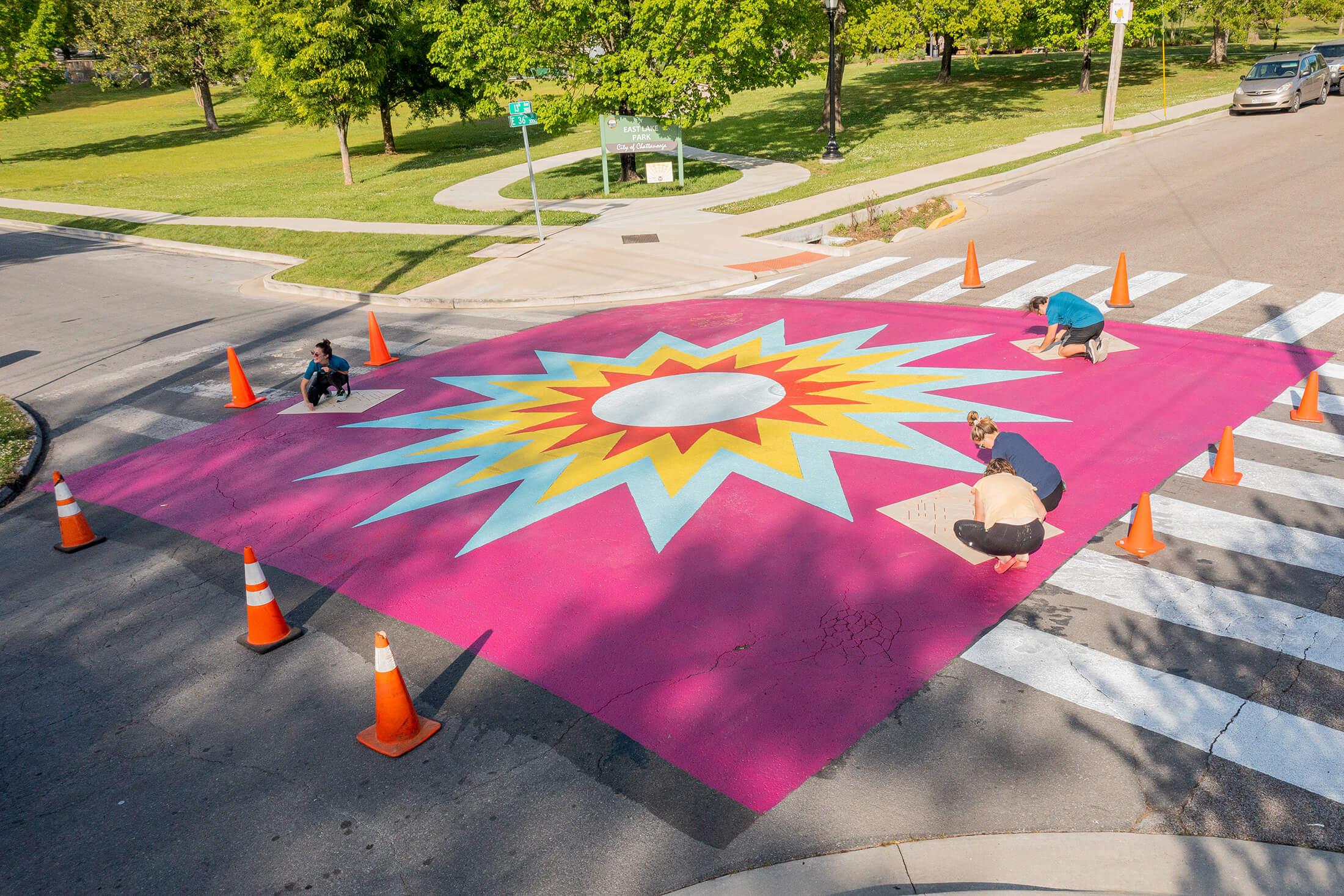 A group of people painting a crosswalk with a sun on it.