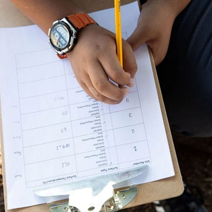 A child is writing on a clipboard with a pencil.