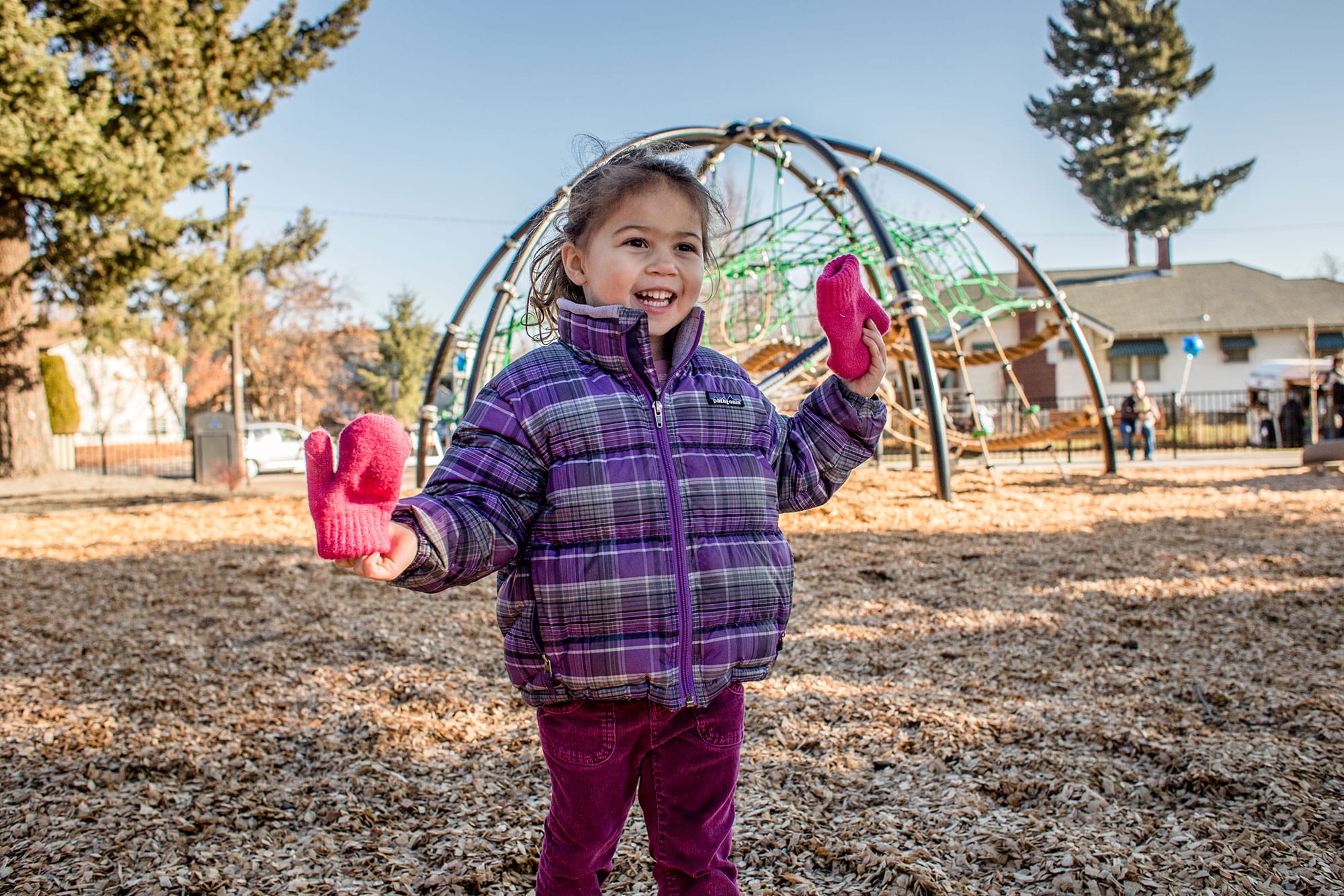 A little girl in a purple jacket standing in a playground.