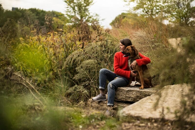 A woman sits on a rock with her dog.