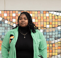 A black woman standing in front of a mosaic wall.