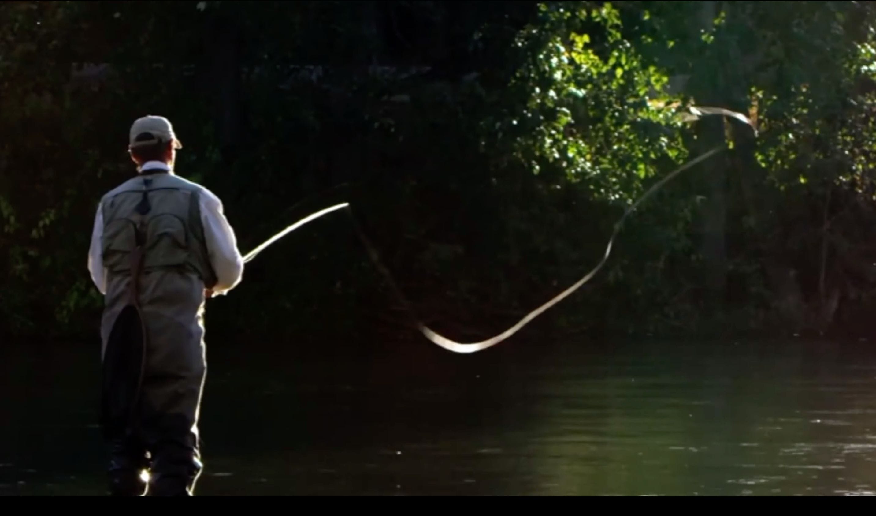 A man is standing in a river with a fly rod.