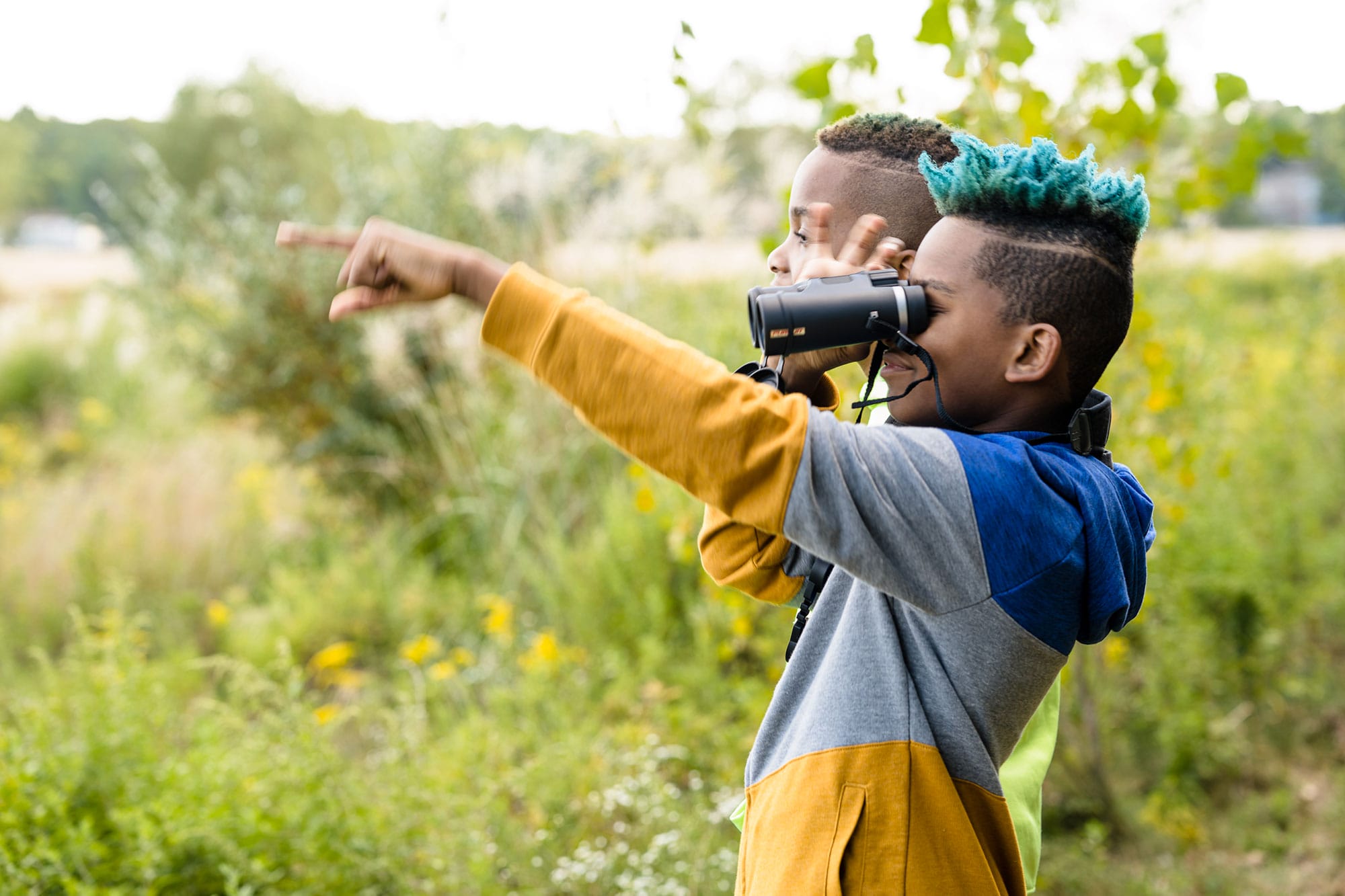 Two boys looking through binoculars in a field.