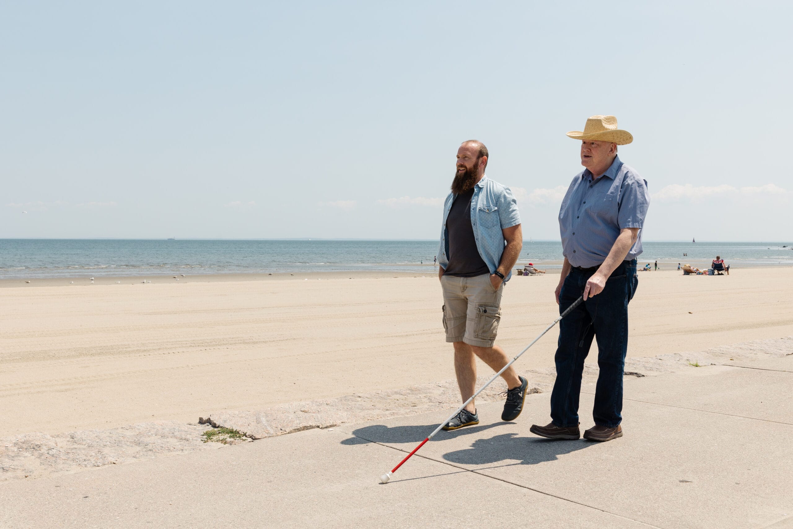 Two men walking on the beach with canes.