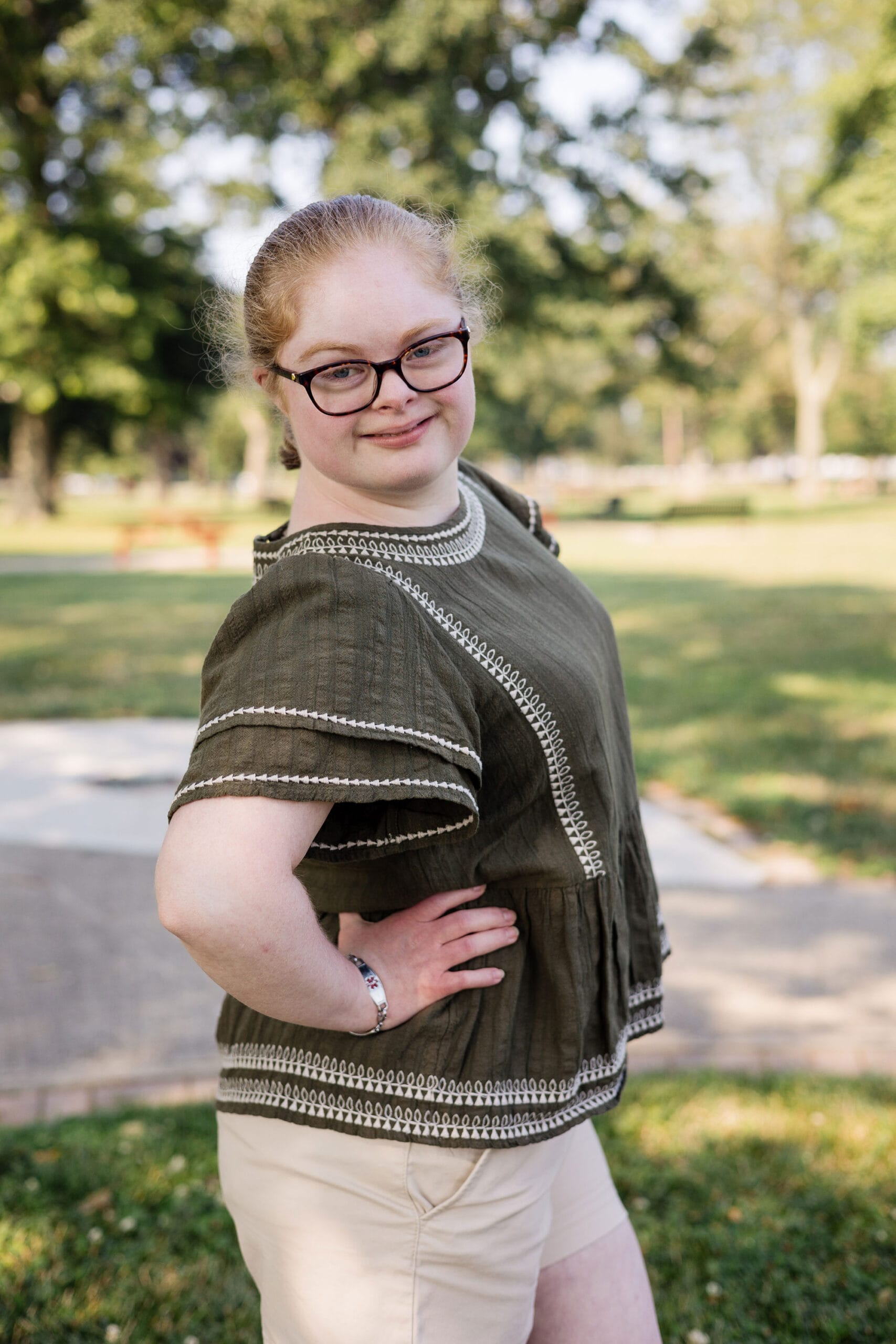 A girl wearing glasses and shorts is posing in a park.