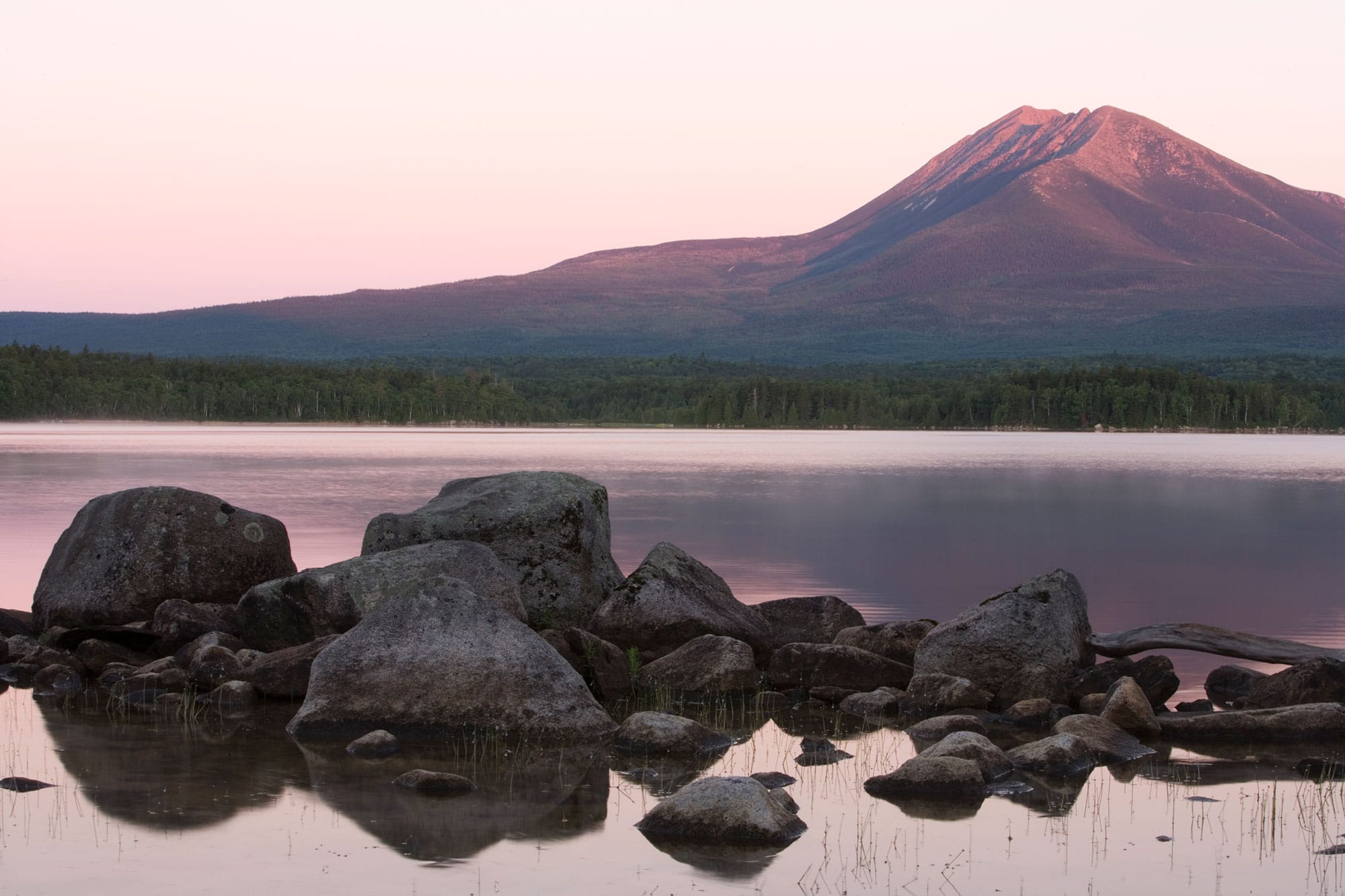 A lake with rocks and a mountain in the background.