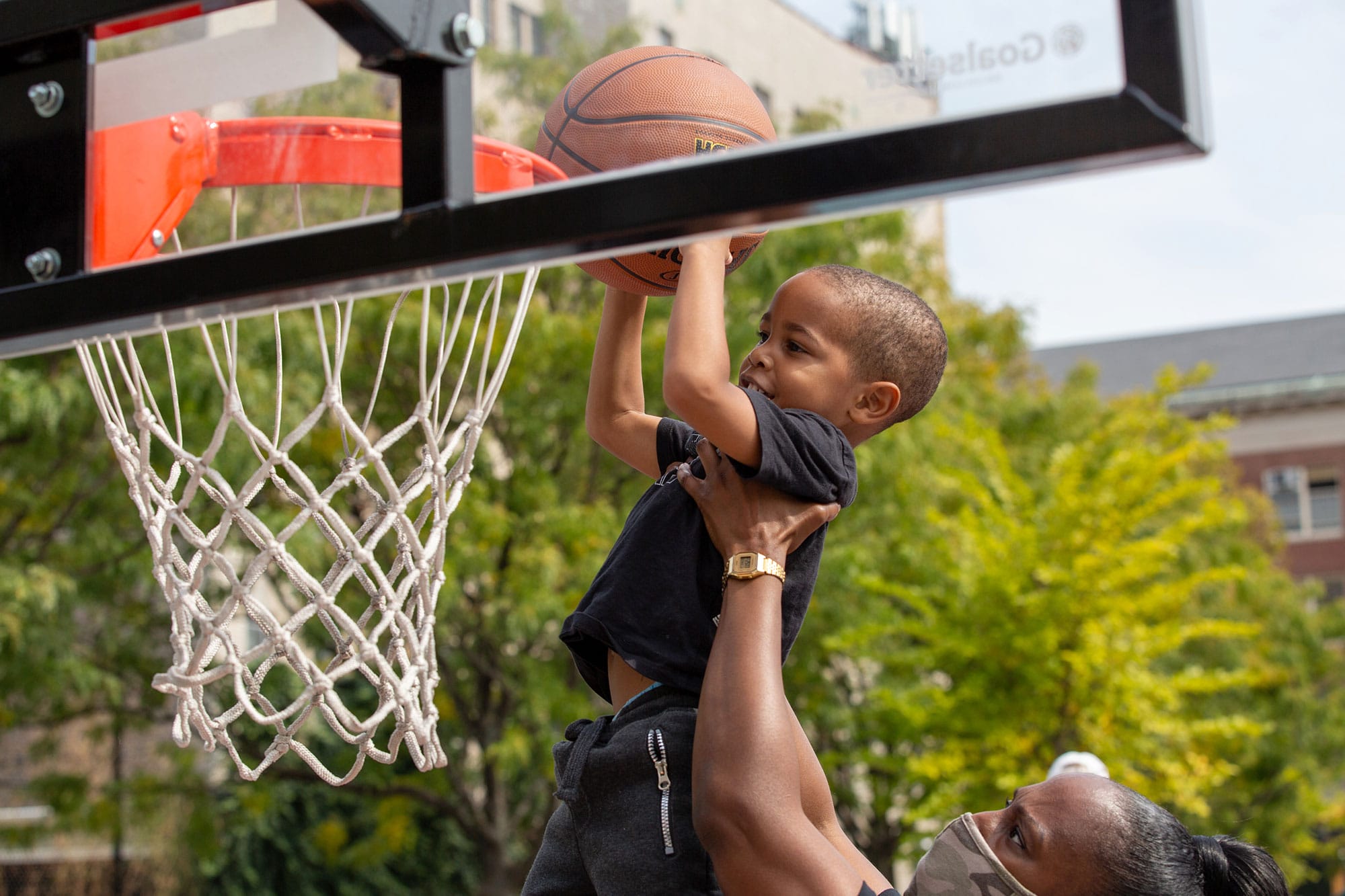 A young boy dunks a basketball in a park.