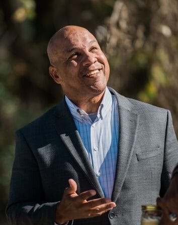 A bald man in a suit is smiling at a group of people.