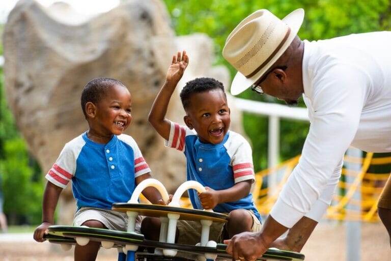 A man is playing with two young boys in a playground.