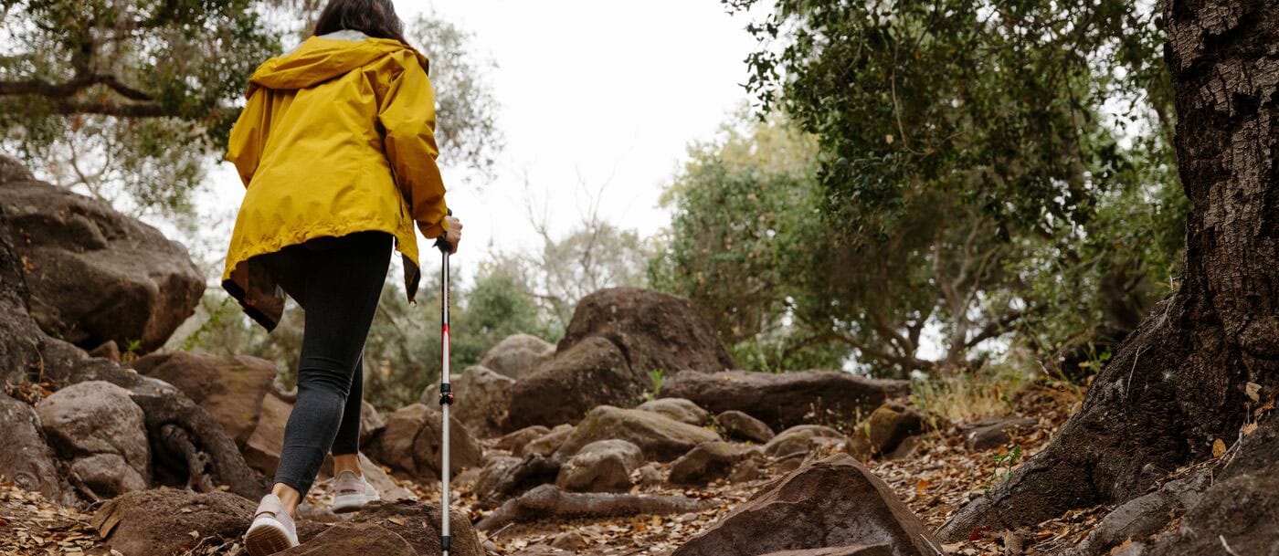 A woman in a yellow jacket walking through the woods.