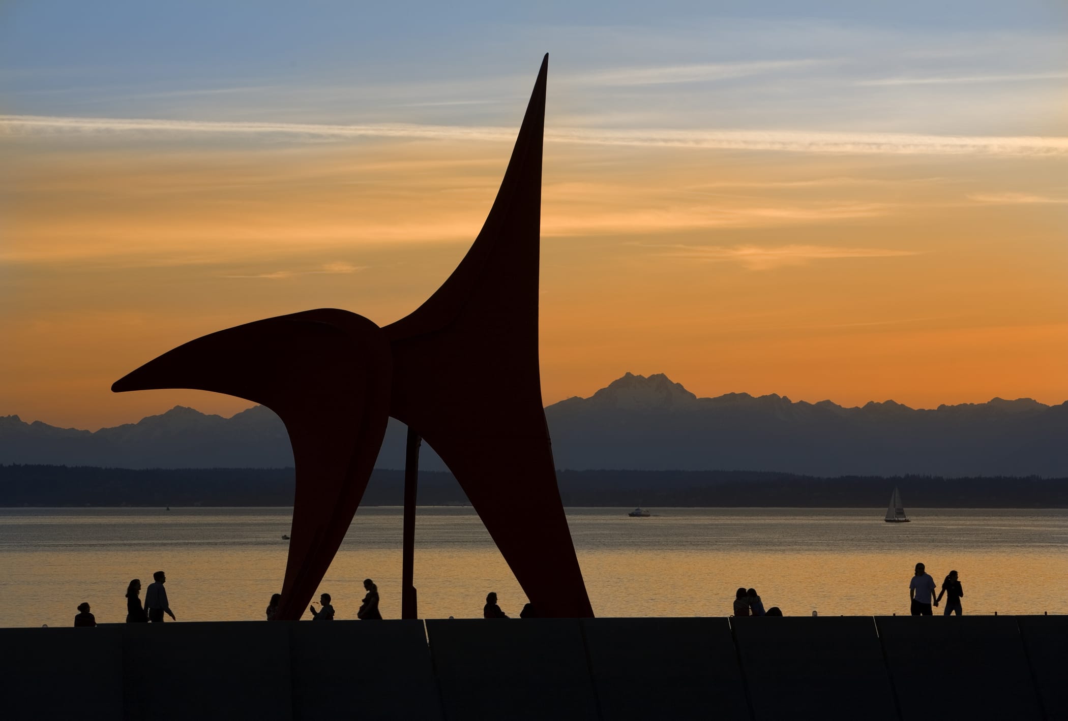 A red sculpture sits on the water at sunset.
