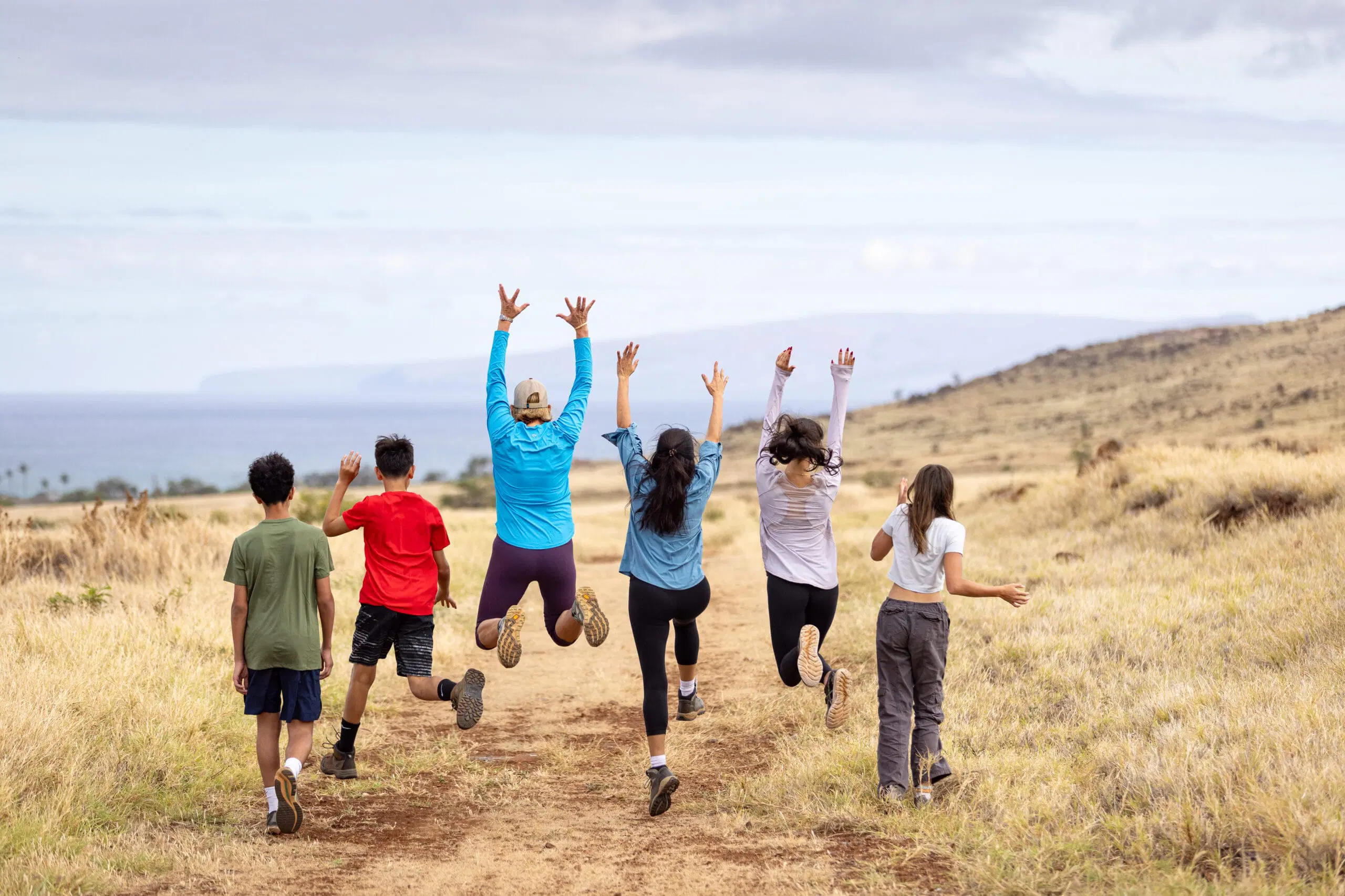 Six people walk down a trail, jumping and skipping