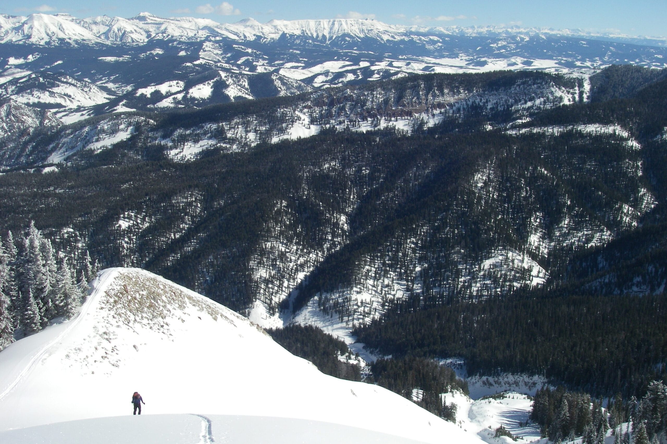 A skier heads up a snowy trail in Wyoming with a big valley and mountains behind them.