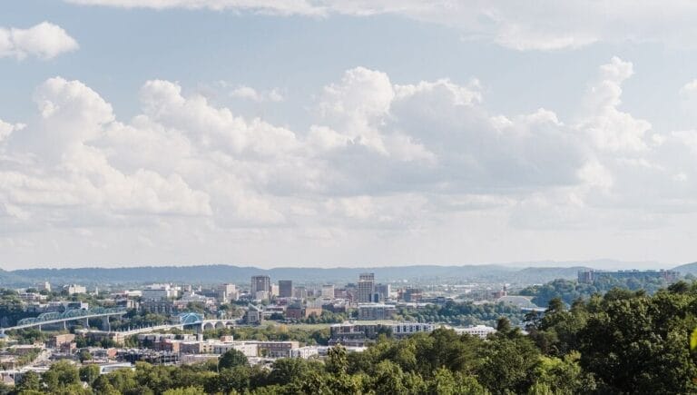 A panoramic view of a cityscape with a mix of buildings, roads, and greenery under a partly cloudy sky.